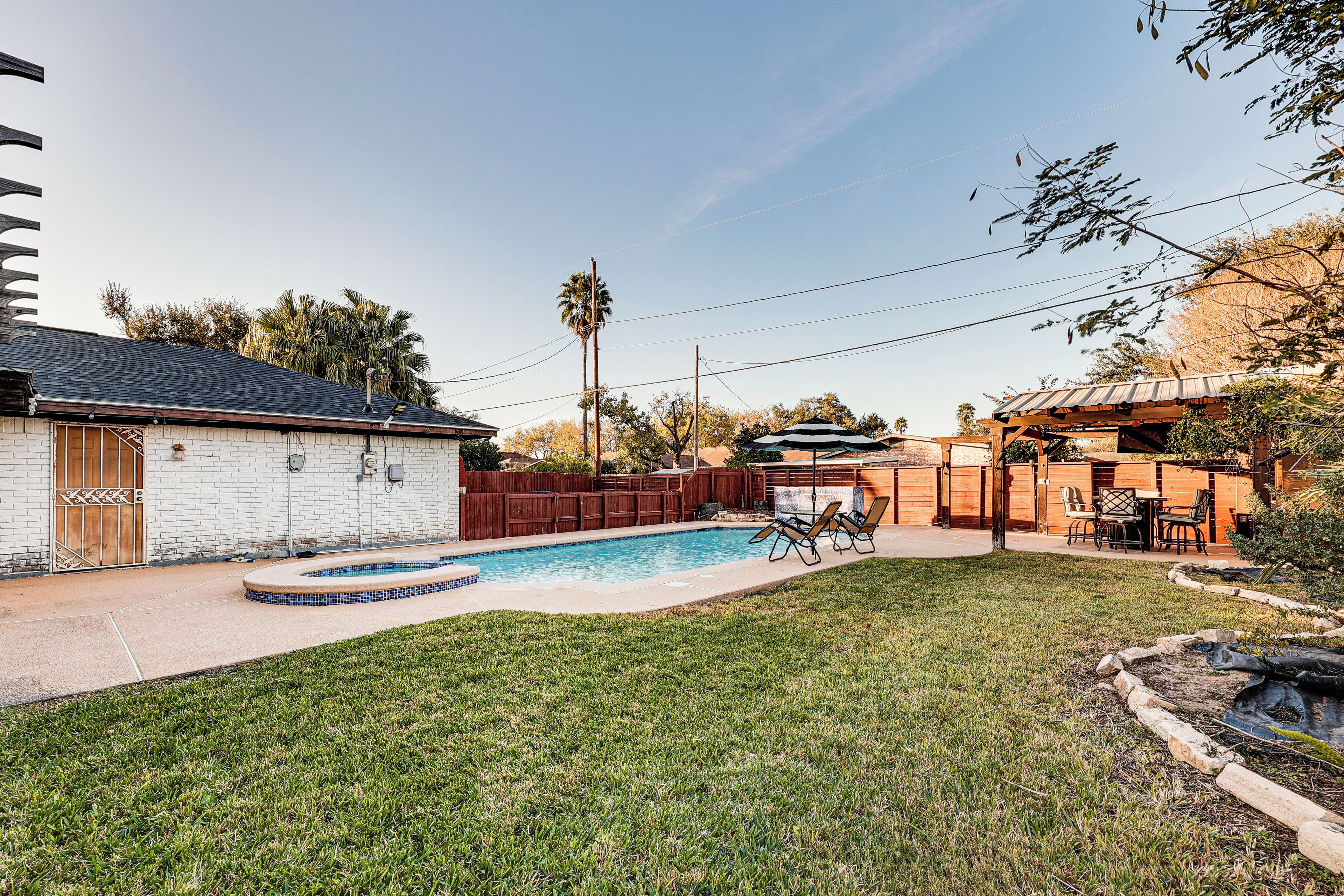 Un patio trasero con piscina, terraza de madera y zona de estar con mobiliario exterior.