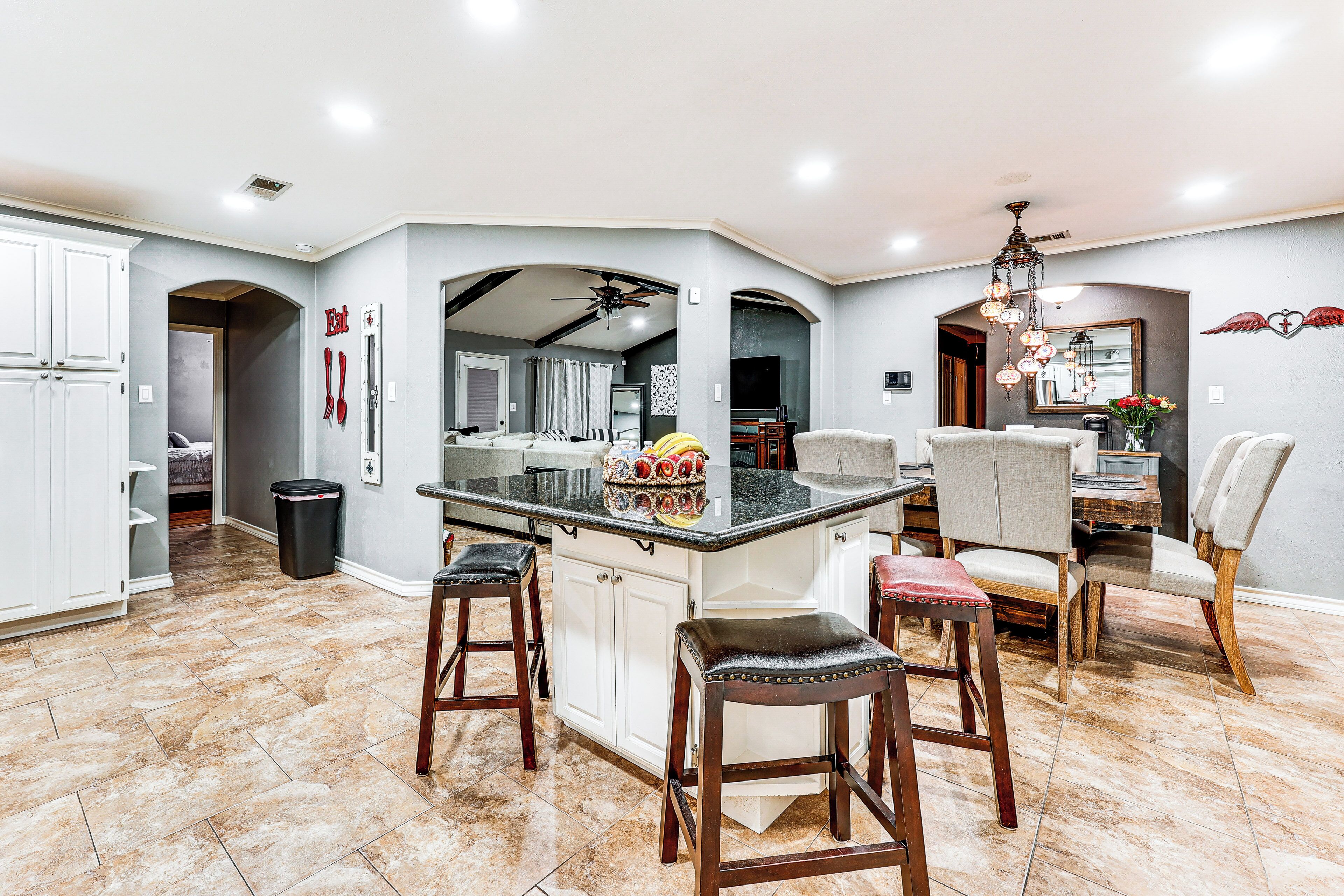 A spacious kitchen with a central island, white cabinetry, and a dining area with chairs and a chandelier.