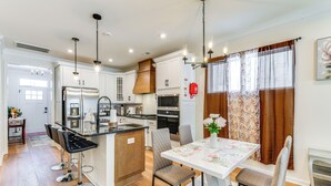 A modern kitchen with a central island, bar stools, and a dining table with chairs. - 12 Mi to Dtwn Richmond: Spacious Home w/ Deck! (Richmond)