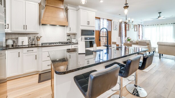 A modern kitchen with white cabinets, a central island with bar stools, and a dining area with a sofa and chairs. - 12 Mi to Dtwn Richmond: Spacious Home w/ Deck! (Richmond)