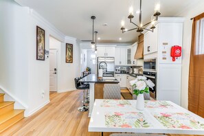 Une cuisine moderne avec des meubles blancs, un plan de travail noir et des appareils en acier inoxydable. On y trouve un coin repas avec une table dressée pour deux personnes et un vase de fleurs.