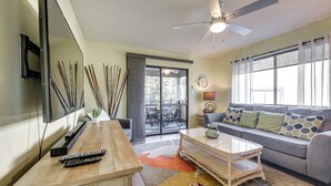 A living room with a sofa, coffee table, and TV. There is a ceiling fan, a window with curtains, and a door leading to an outdoor area. - 1 Mi to Coast: Myrtle Beach Condo w/ Balconies! (Myrtle Beach)