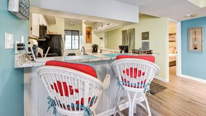 A kitchen with a bar area, two wicker chairs with red cushions, and a dining table. - 1 Mi to Coast: Myrtle Beach Condo w/ Balconies! (Myrtle Beach)