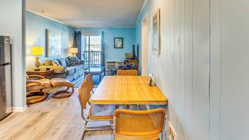 A dining area with a wooden table and wicker chairs, a sofa, and a small kitchen area with a refrigerator.