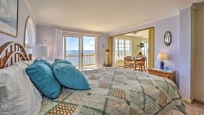 A bedroom with a large bed, a view of the sea through a sliding door, and a dining area with a table and chairs. - Ocean-view Cape Cod Condo in Truro! (North Truro)