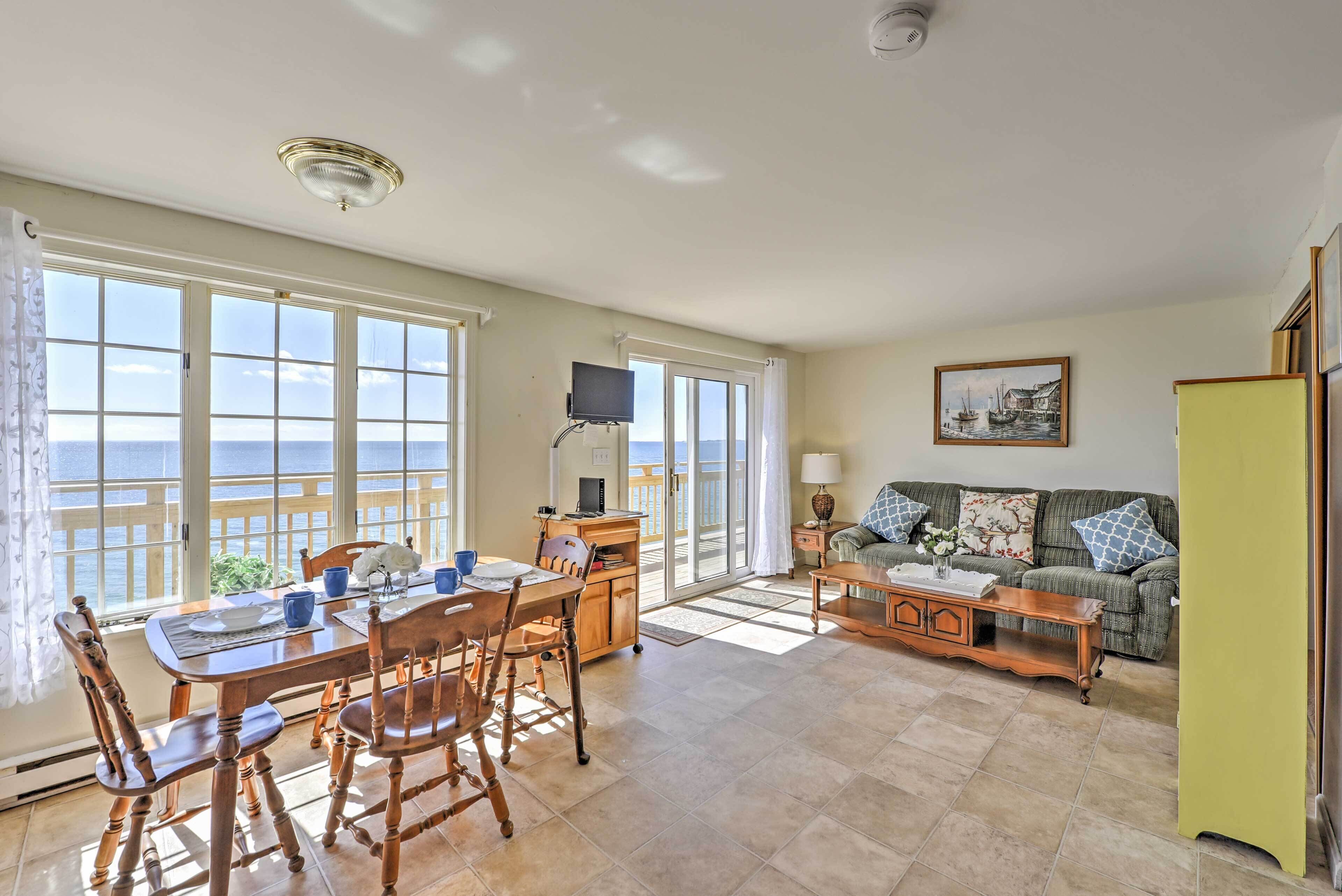 A spacious living room with a dining area, large windows, a television, and a sofa with cushions.