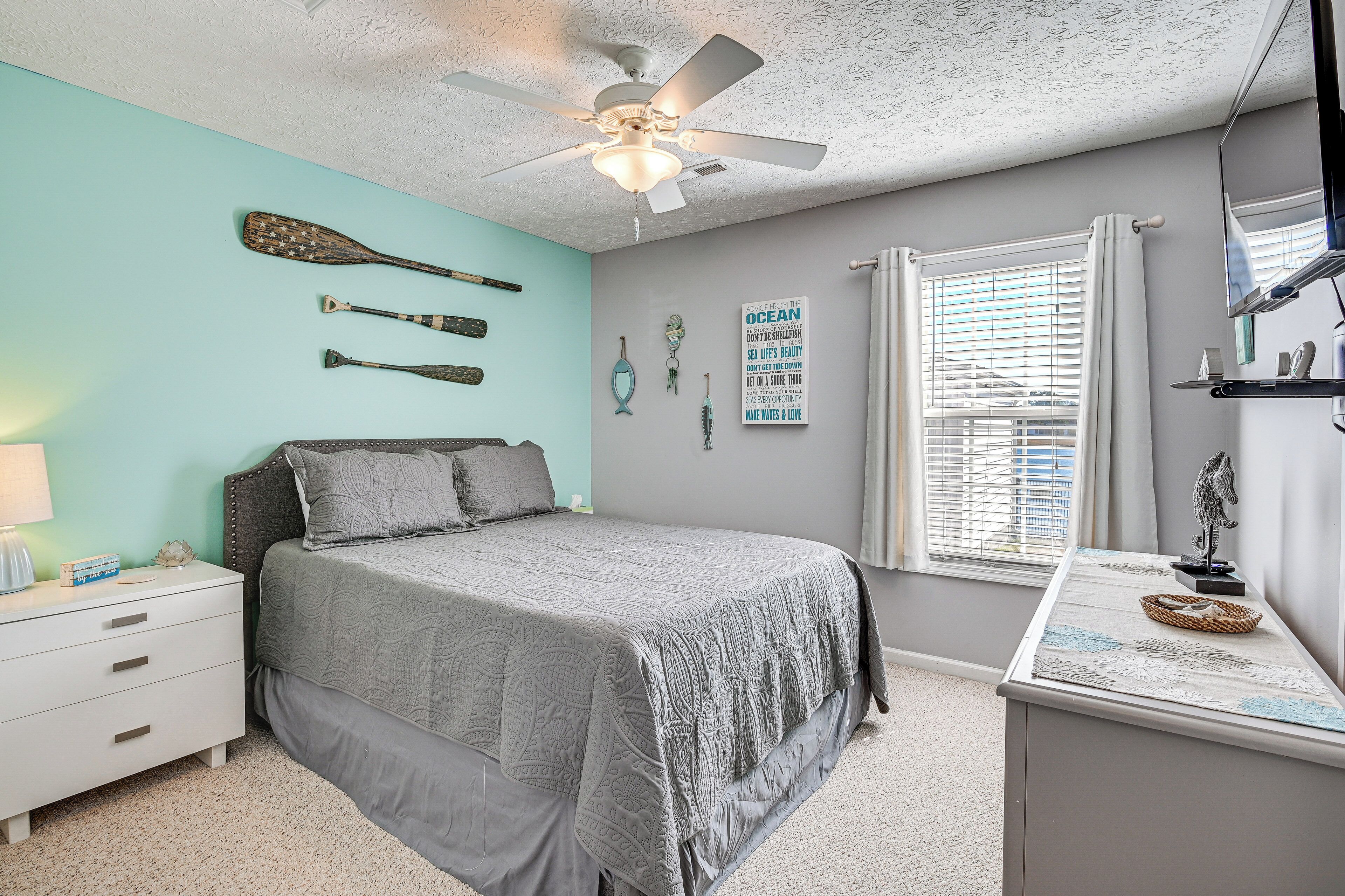 A bedroom with a bed, a nightstand, a ceiling fan, and wall decorations.