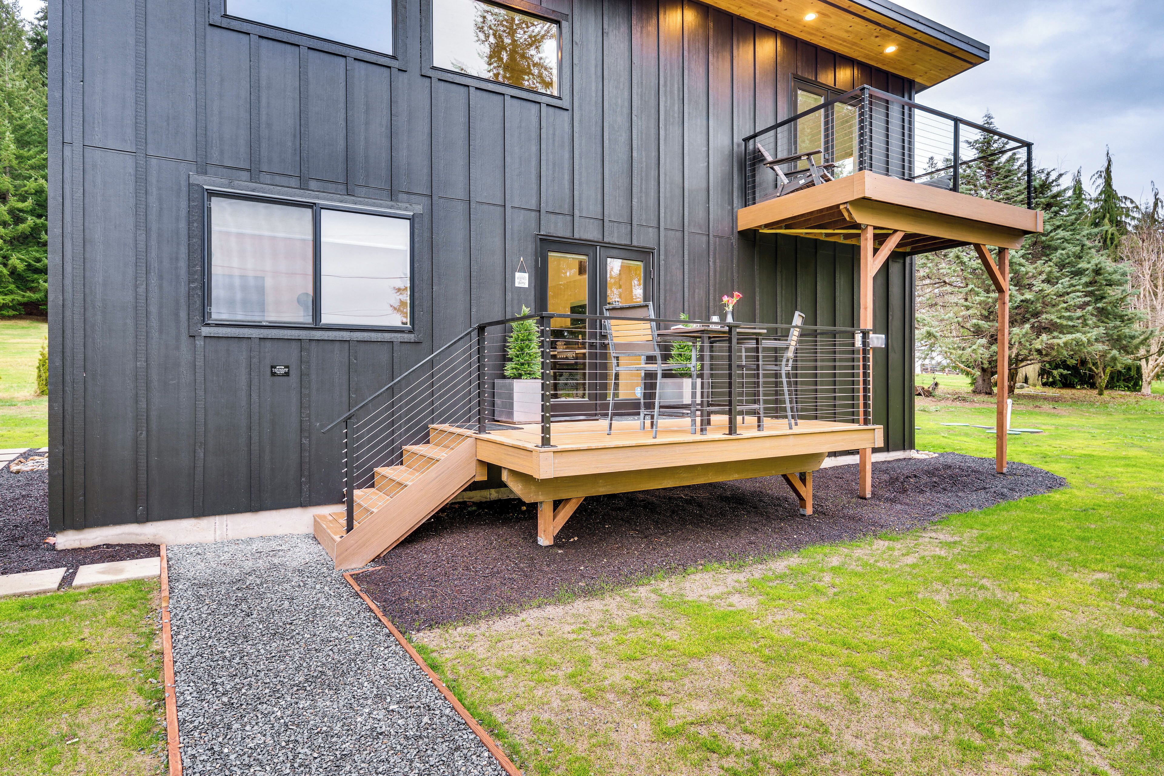 A modern two-story house with a wooden deck, a staircase, and a balcony.