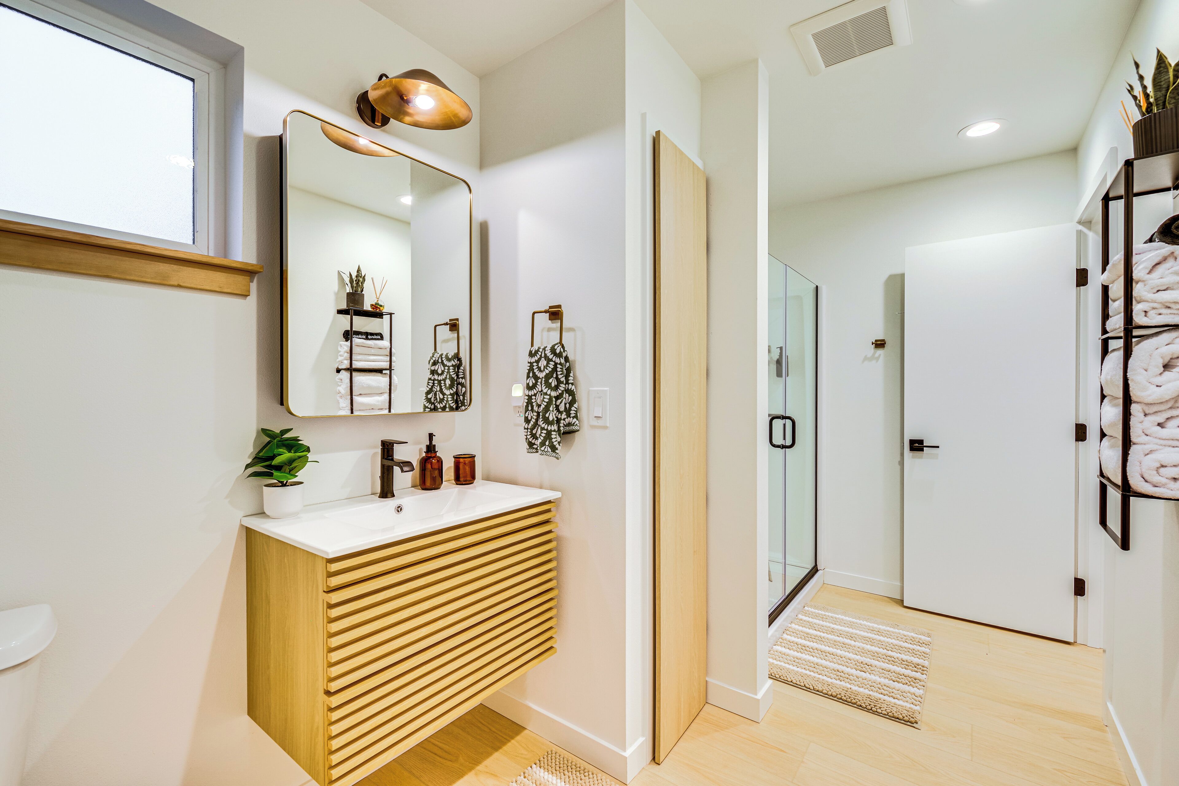 A modern bathroom with a wooden vanity, a large mirror, and a glass shower door.