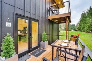 Un edificio moderno con terraza de madera, felpudo y mesa de comedor para dos.