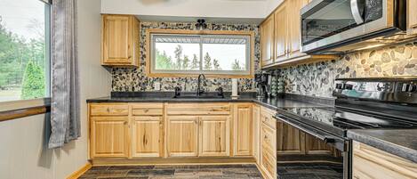 A kitchen with wooden cabinets, a stone backsplash, a large window, and a built-in microwave.