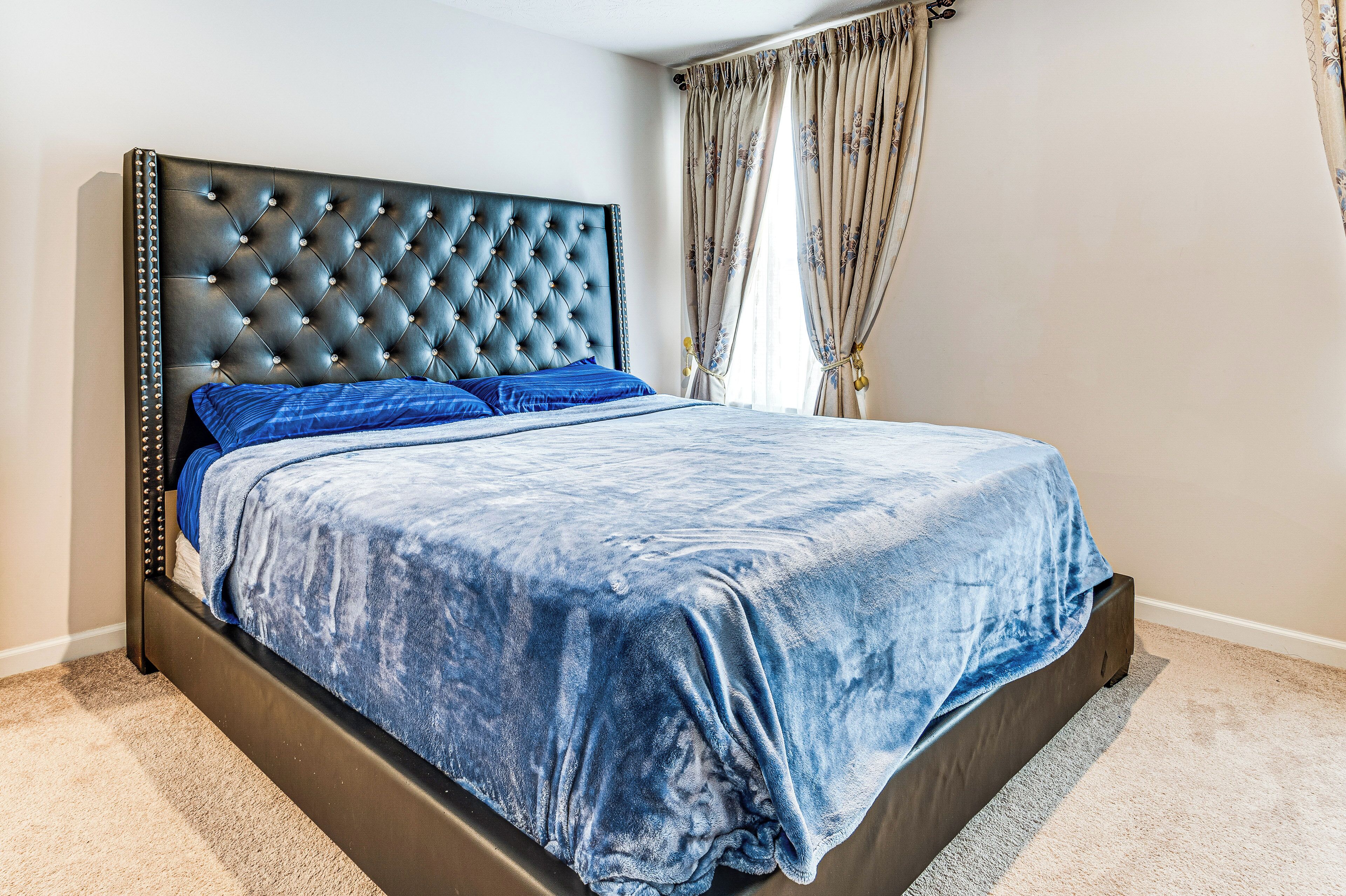 A bed with a tufted headboard, a blue bedspread, and matching pillows.