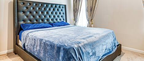 A bed with a tufted headboard, a blue bedspread, and matching pillows.