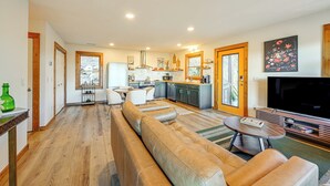 Un salon moderne avec un grand canapé d’angle beige, un téléviseur à écran plat et une cuisine en arrière-plan.