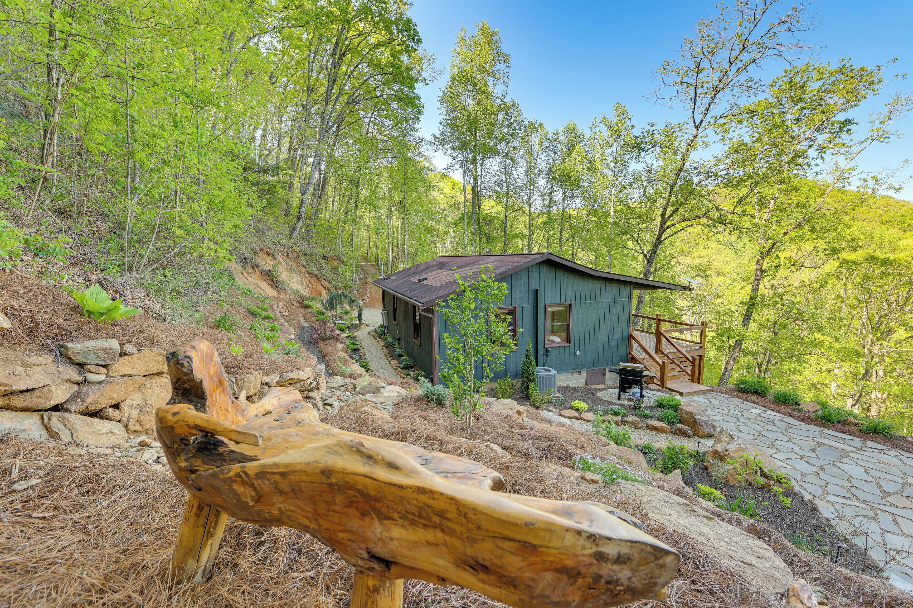 A cabin with a stone pathway leading to it, surrounded by trees and a wooden sculpture.