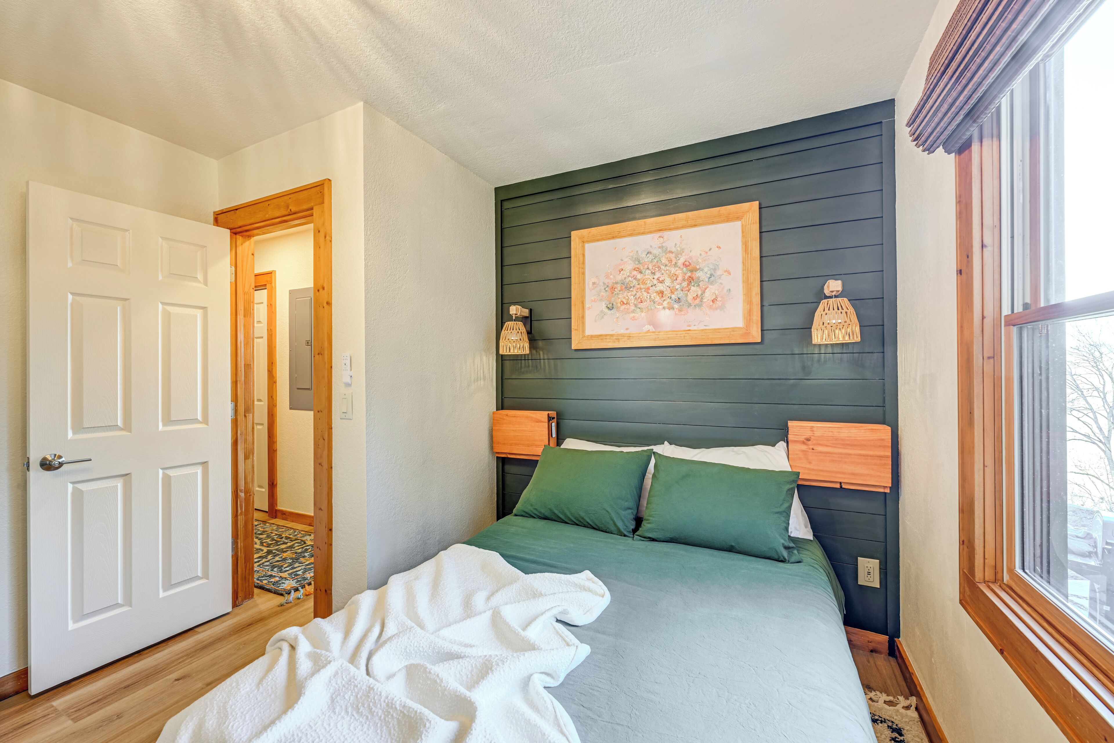 A bedroom with a bed, a door, a window, and a framed picture on the wall.