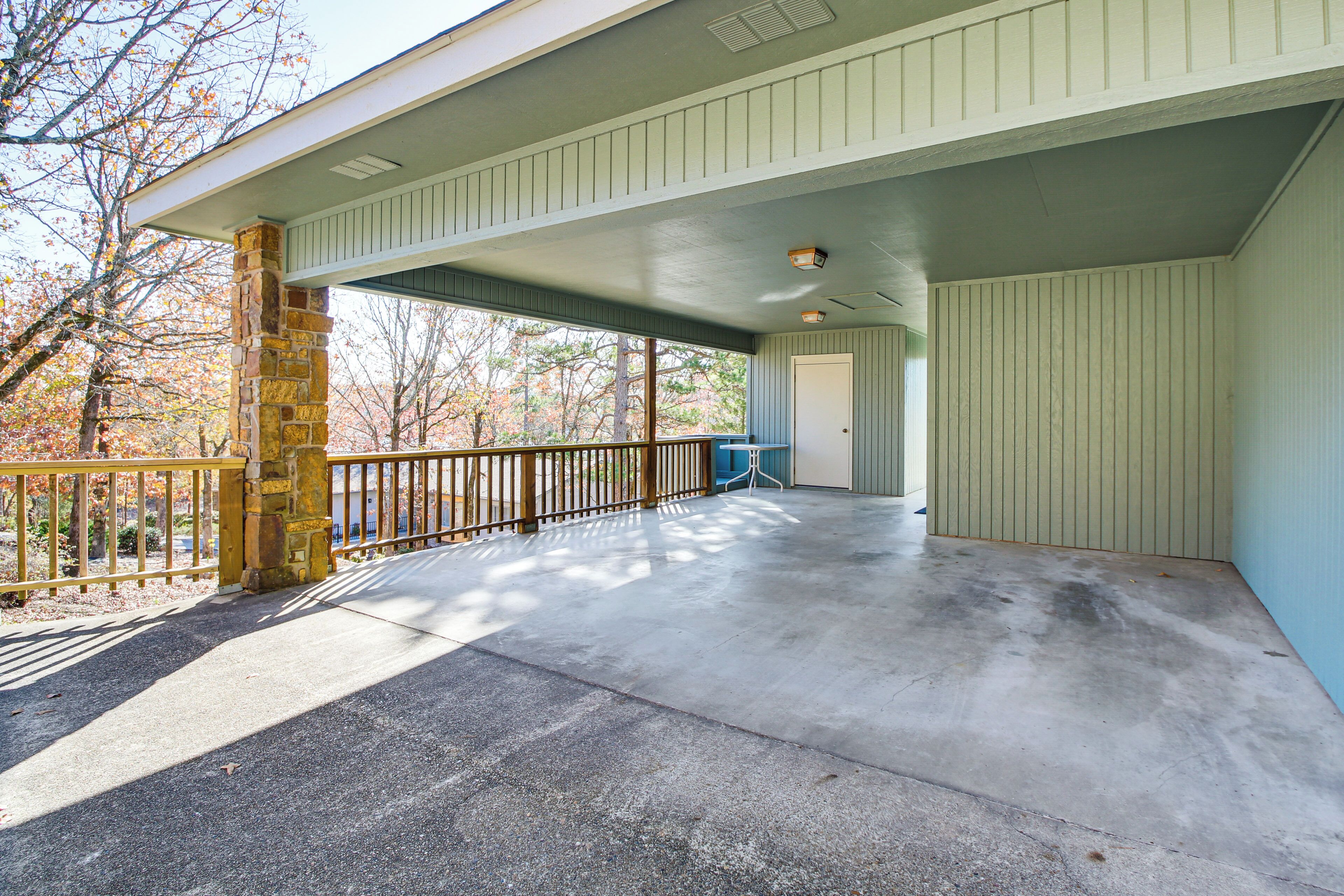 A covered outdoor area with a concrete floor, a stone pillar, and a wooden railing.