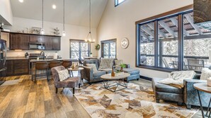 A spacious living area with a large window, a kitchen with dark wooden cabinets, and a dining area with a round table and chairs. - Hot Tub & Trail Access: Black Hills, Rally Stay! (Lead)