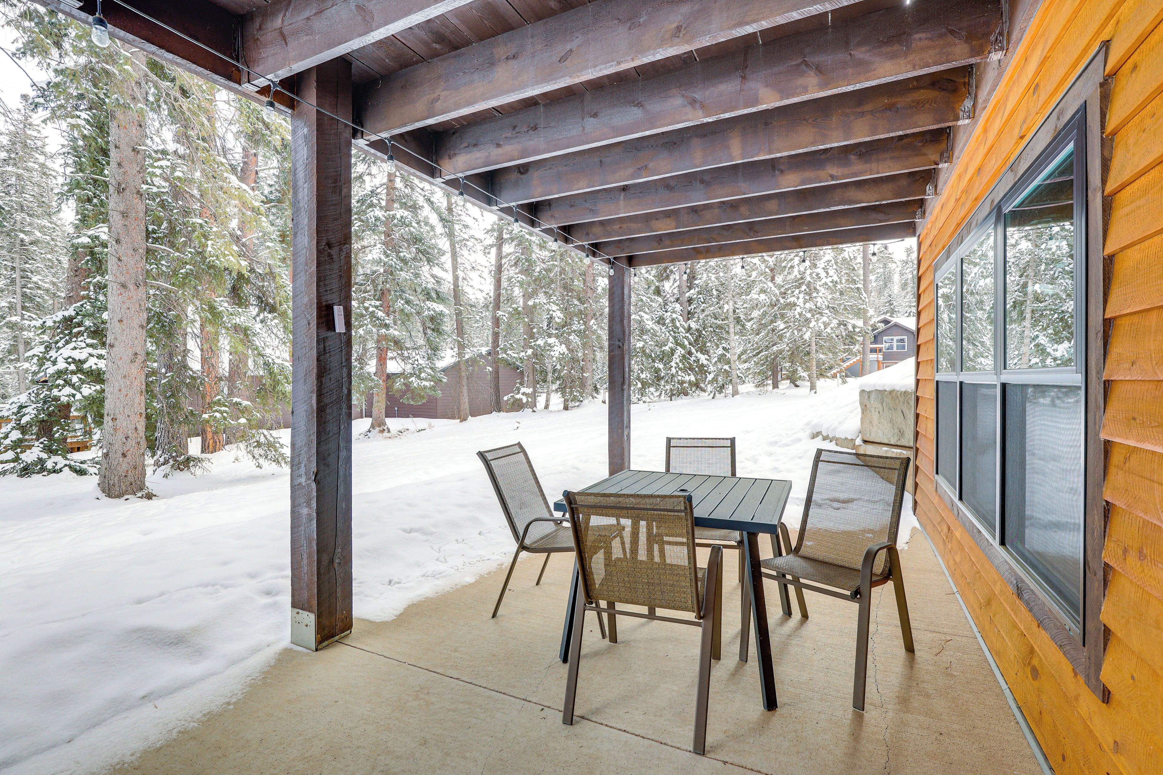 A covered patio with a table and chairs, overlooking a snowy forest.