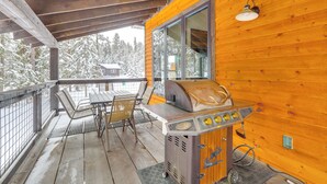 A wooden cabin with a covered porch, a grill, a table with chairs, and a view of snow-covered trees. - Hot Tub & Trail Access: Black Hills, Rally Stay! (Lead)