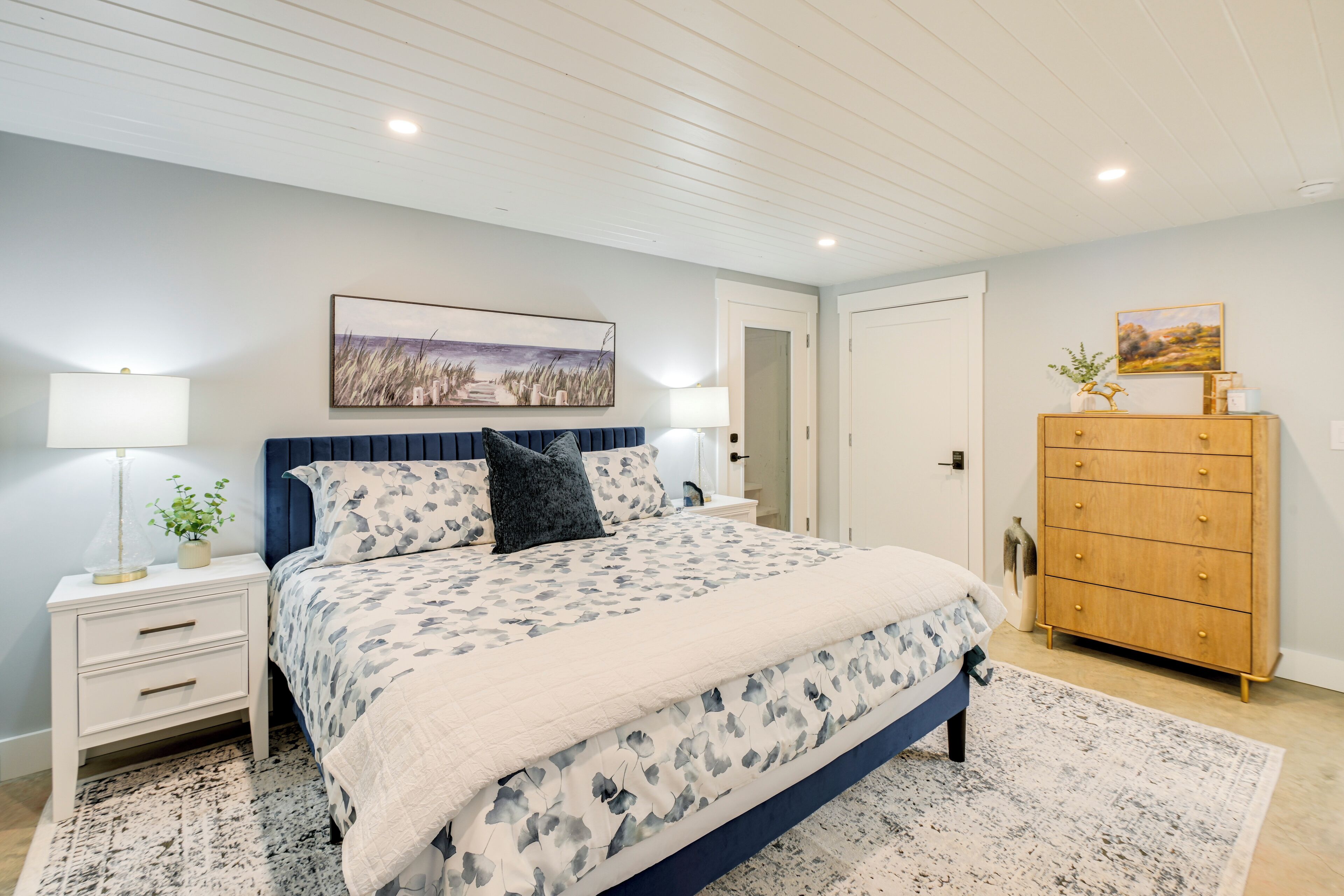 A bedroom with a bed, nightstands, a dresser, and a painting on the wall.