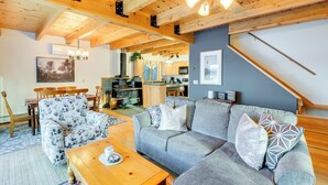 A cozy living room with a wooden ceiling, a grey sofa, a floral armchair, and a wooden coffee table.