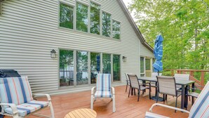 A covered deck with outdoor furniture, including chairs and a table, and a view of a house with large windows.