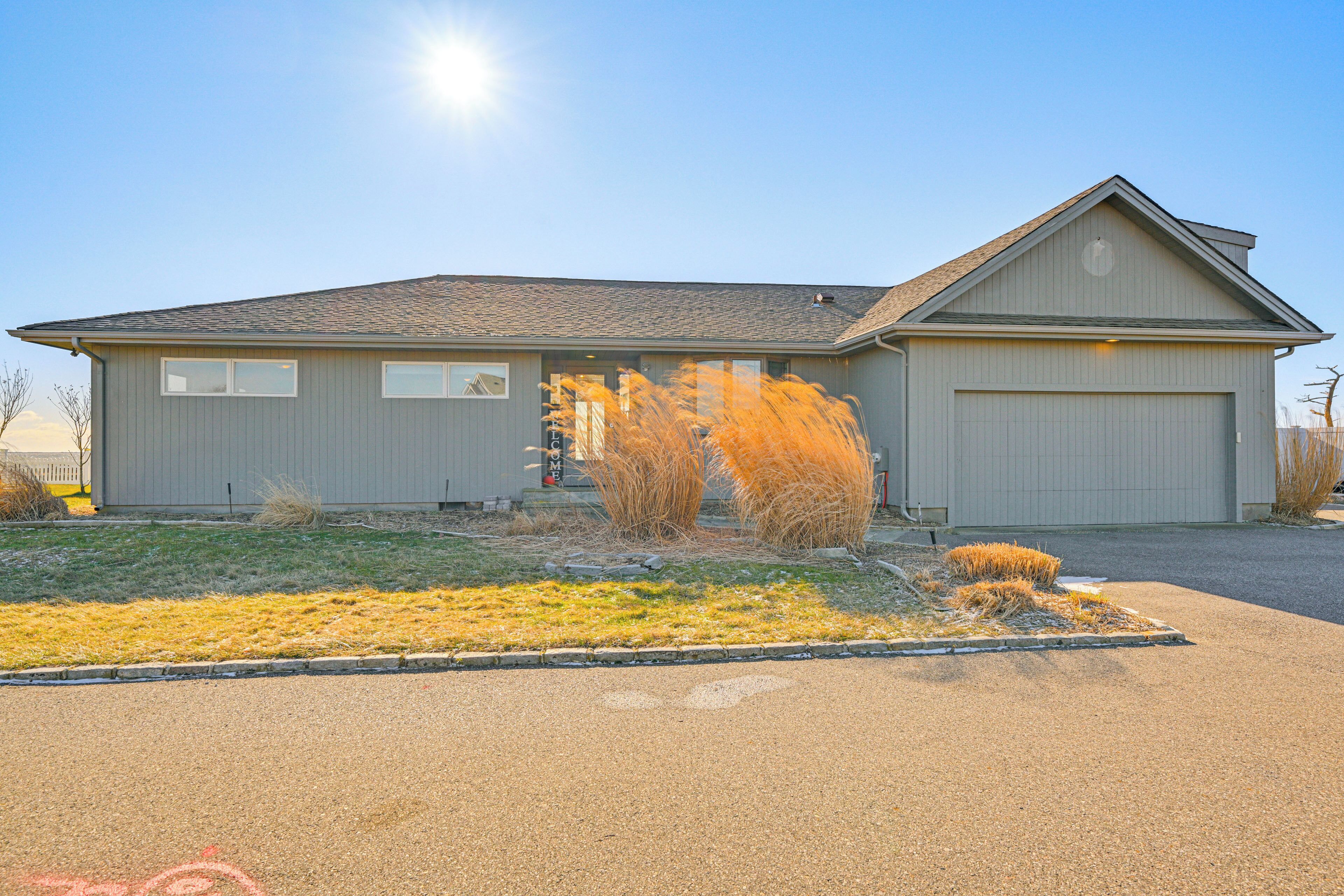 A single-story house with a garage, a front yard with dry grass, and a clear sky.