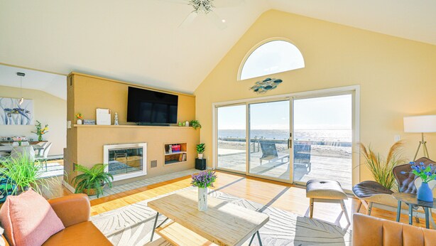 A spacious living room with a large window, a fireplace, and a view of the beach. - Bayfront Home in Patchogue w/ Deck & Fishing Dock (Patchogue)