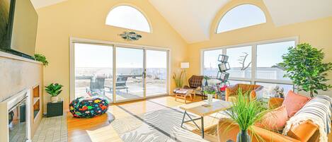 A spacious living room with a fireplace, large windows, and a view of the beach.