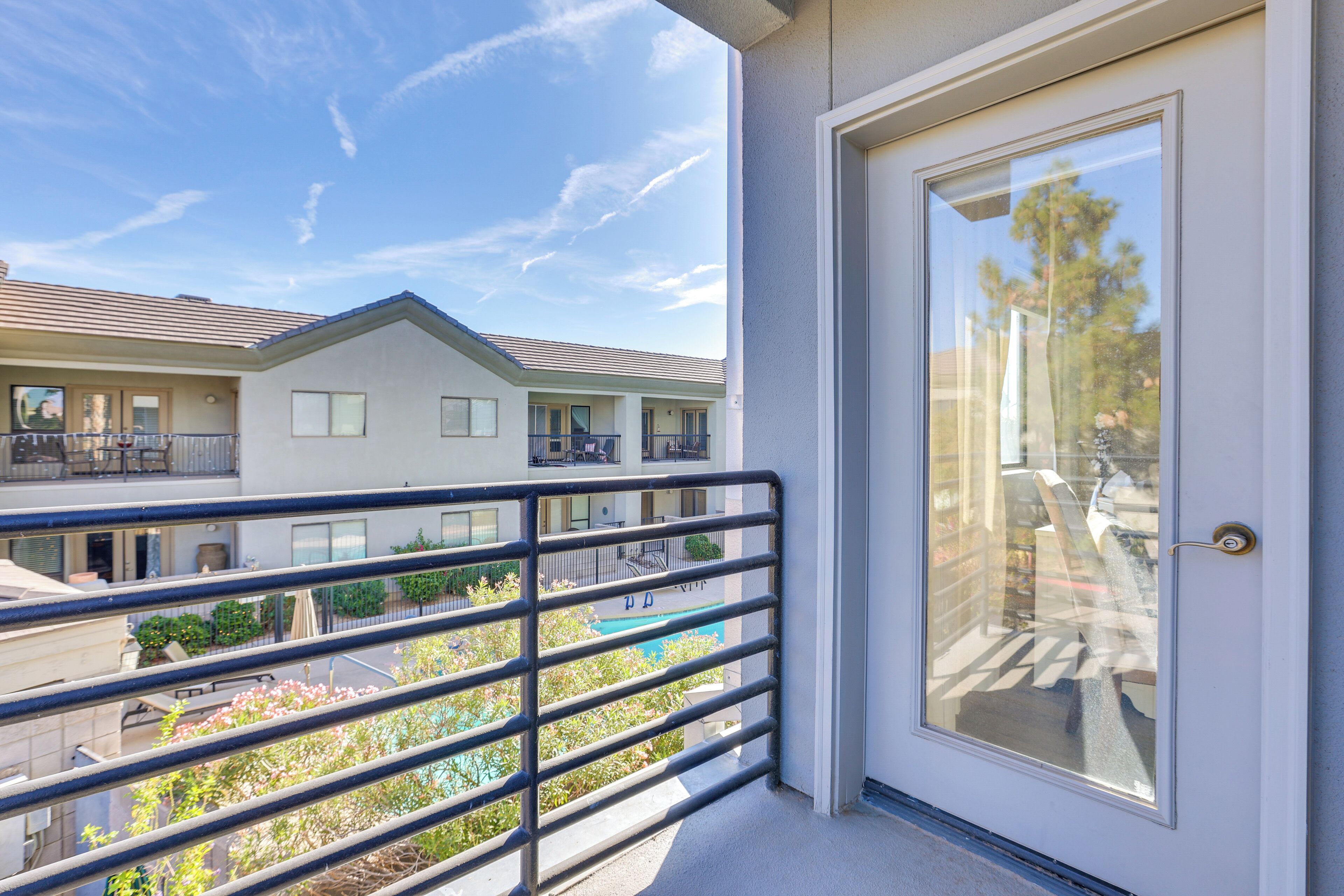 A balcony with a metal railing overlooking a residential area, a door with a glass panel, and a clear blue sky.