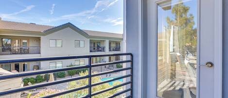 A balcony with a metal railing overlooking a residential area, a door with a glass panel, and a clear blue sky.