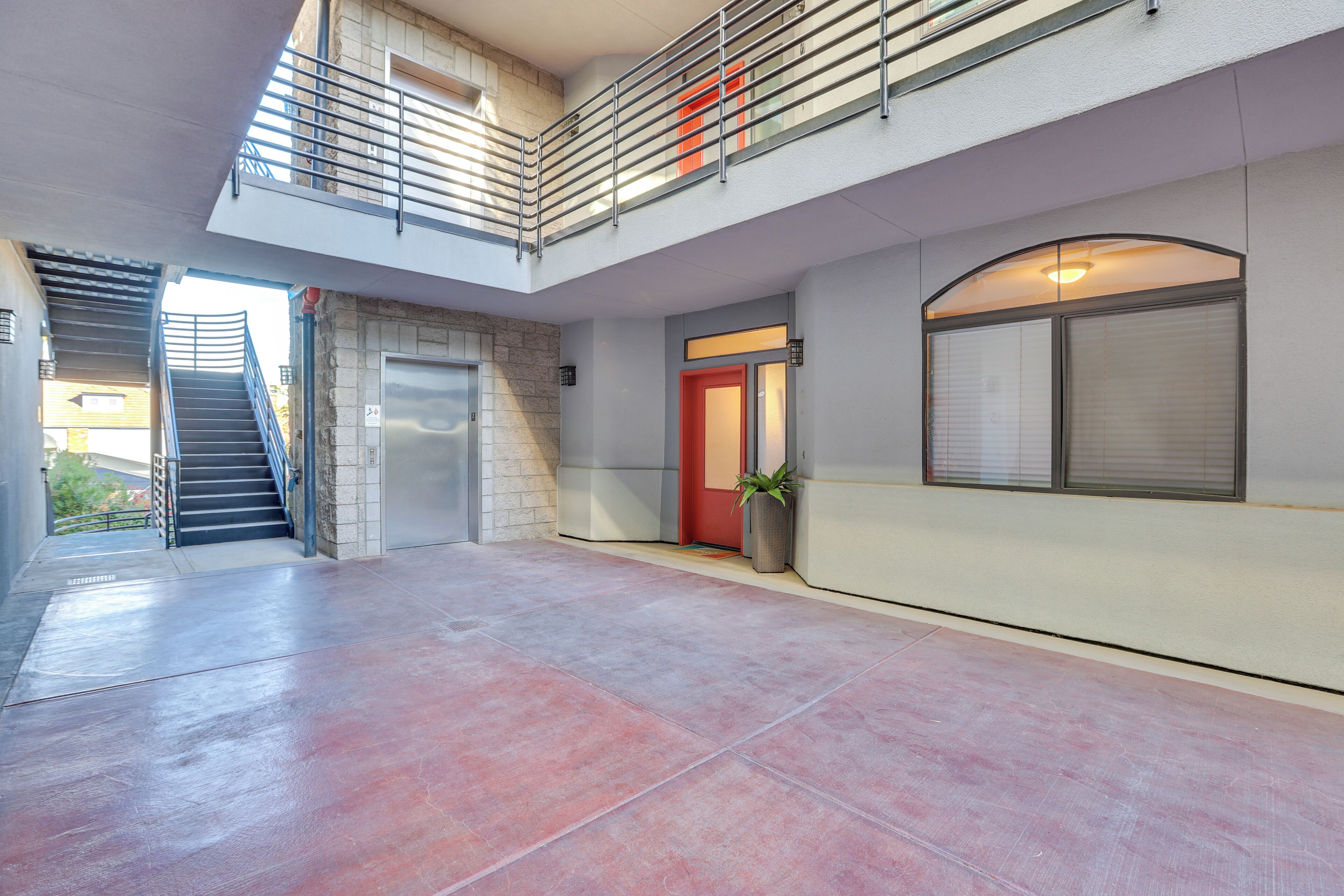 A spacious indoor area with a red door, a staircase, and a large window.