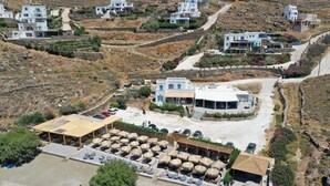 Resort costeiro com edifícios brancos, zona de praia com espreguiçadeiras e área de estar coberta.