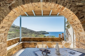 A stone archway leading to a terrace with a table, chairs, and a view of the sea. - Villa 'Tinos Traditional Sea Side' with Sea View, Wi-Fi and Air Conditioning (Agios Romanos)