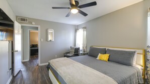 Una camera da letto con un letto, una ventola a soffitto, un comodino e una finestra con tende.
