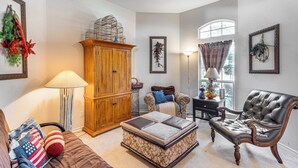 A living room with a wooden cabinet, a leather armchair, a sofa with American flag pillows, and a floor lamp.