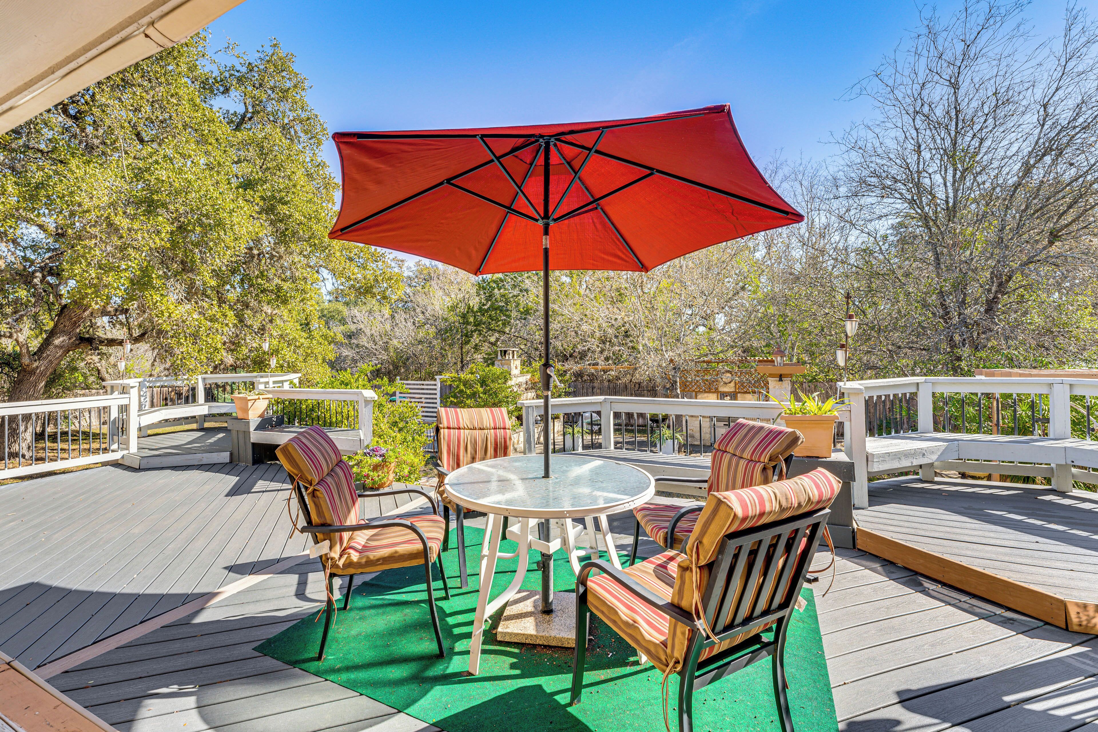 A deck with a round table and chairs, a red umbrella, and a white railing.