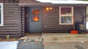 Une cabane en rondins avec une porte en bois, une fenêtre ornée d’un rideau rouge et un petit porche.