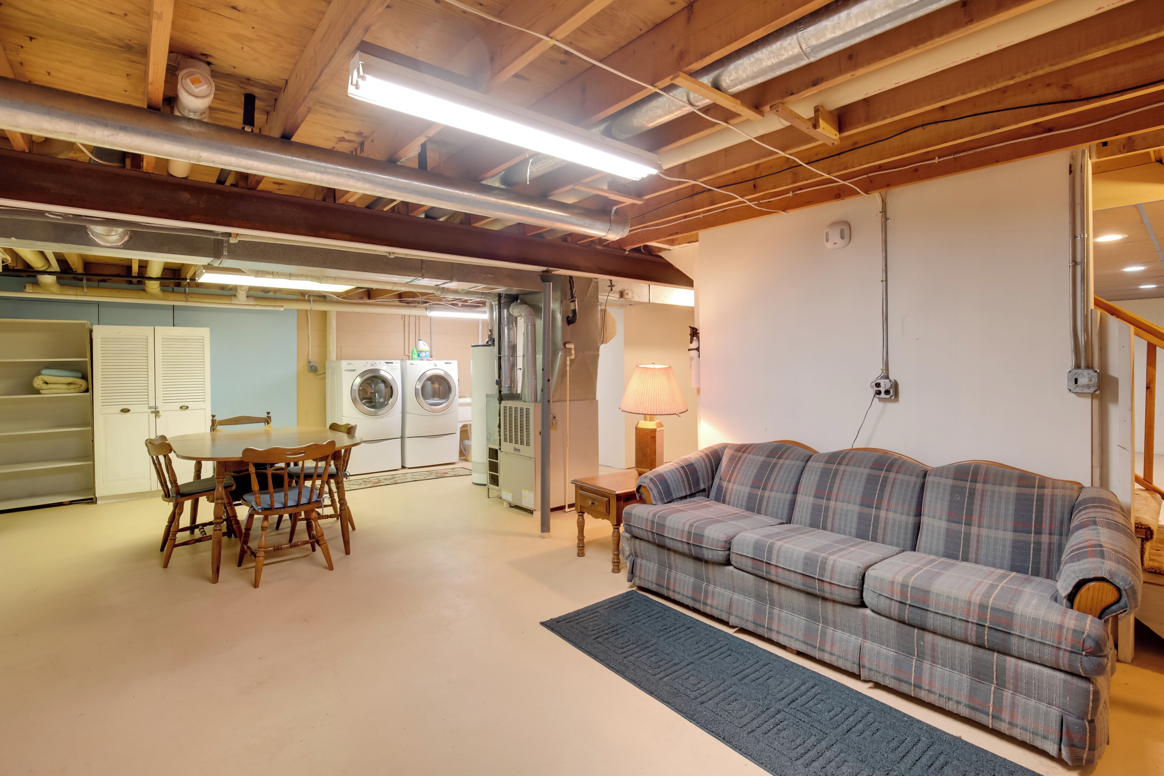 A room with a plaid sofa, wooden dining table, chairs, a washing machine, and a lamp.