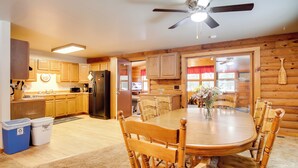 L’intérieur d’une cabane en bois comprend une table à manger, des chaises, un réfrigérateur et un ventilateur de plafond.