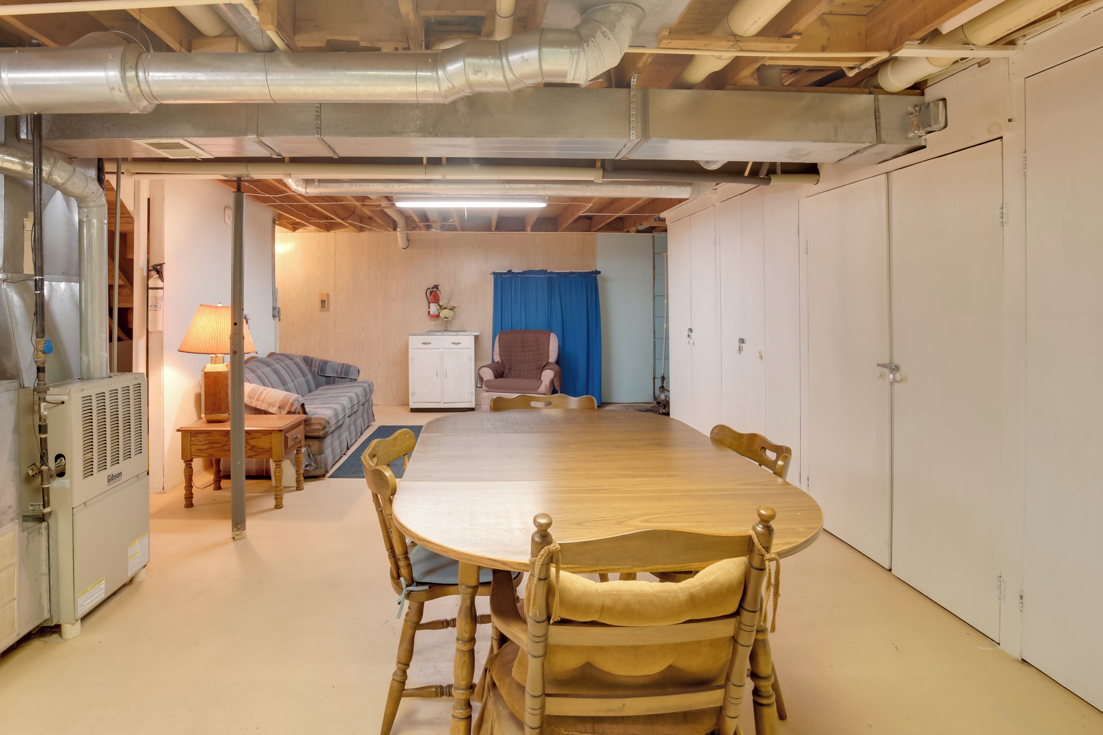 A room with a wooden dining table, chairs, a sofa, a lamp, and a small cabinet.