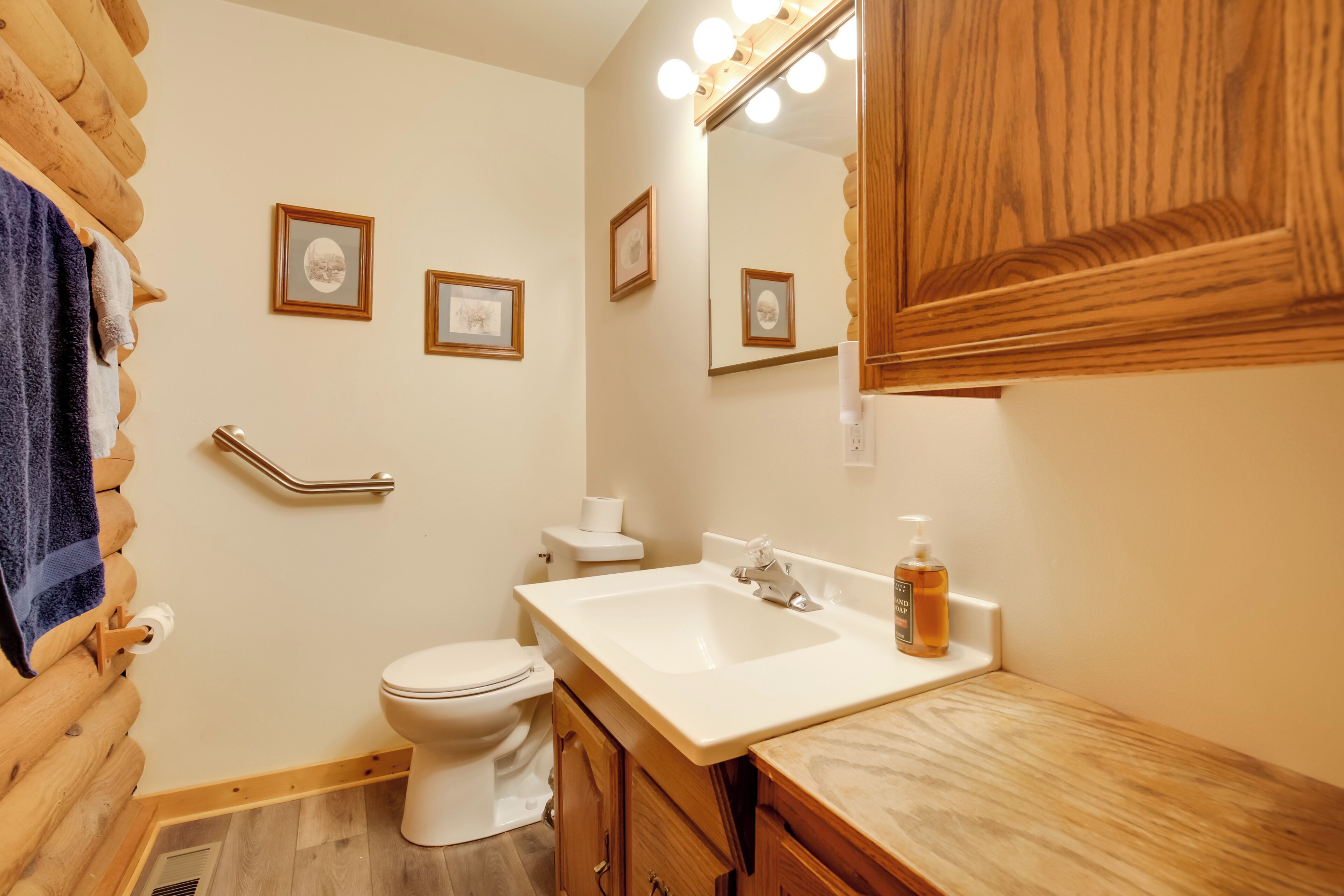 A bathroom with a wooden vanity, a white sink, a mirror, and framed pictures on the wall.