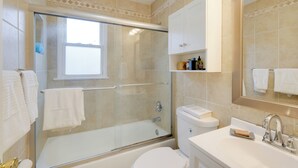 Une salle de bain moderne avec une douche à parois de verre, des toilettes blanches, un lavabo avec un porte-savon et un miroir au-dessus du lavabo.