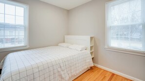 Une chambre à coucher avec un lit, deux fenêtres et un luminaire au plafond.