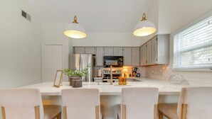 Une cuisine moderne dotée d’un îlot central, de luminaires suspendus et offrant une vue sur l’extérieur.