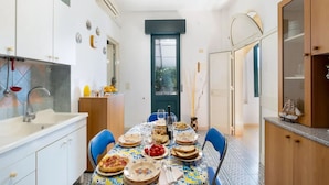 A modern kitchen with white cabinets, a dining table set for four, and a view through a door to the outdoors.