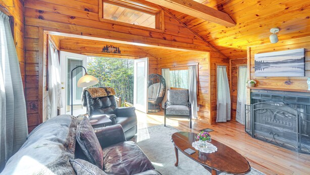 Ein gemütliches Blockhaus-Interieur mit Holzbalkendecke, Kamin, einer Couch, einem Sessel und einem Esstisch.