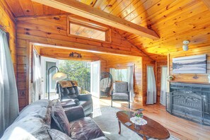 A cozy cabin interior with a wooden ceiling, a fireplace, a sofa, a chair, and a dining table. - Cabin w/ Deck & Mountain Views Near Gatlinburg! (Cosby)