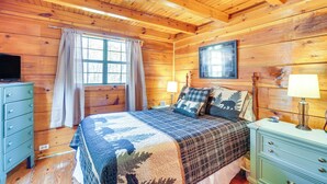 Ein Schlafzimmer einer Holzhütte mit Bett, Kommode, Lampe und Fernseher auf der Kommode.
